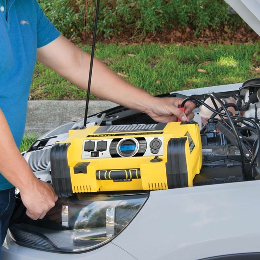 Stanley BC8S portable power station on car hood, jump-starting a vehicle, yellow and black unit.