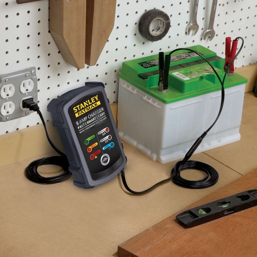 STANLEY BC8S battery charger connected to a car battery on a workshop bench, angled view.