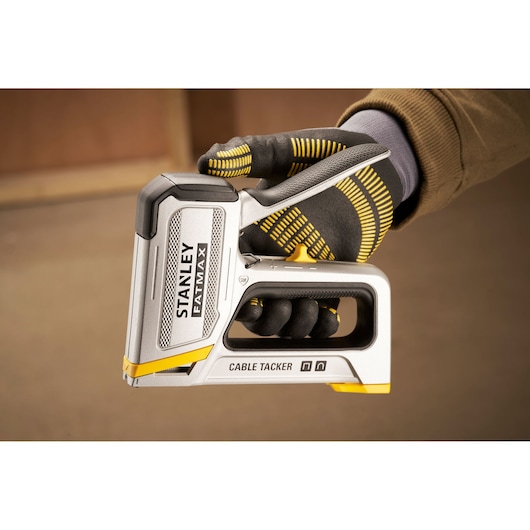 Stanley FATMAX FMHT70100 cable tacker held in gloved hand, silver and yellow design, side angle.