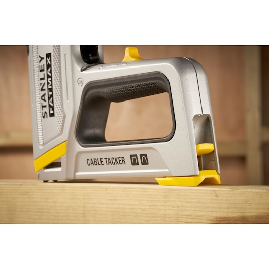 Stanley FMHT70100 cable tacker with silver and yellow finish, side angle on wooden surface.