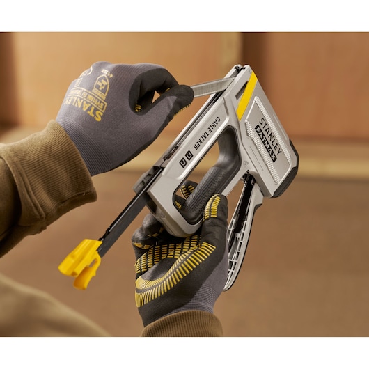 Photo of STANLEY FMHT70100 cable tacker being loaded by gloved hands, silver and yellow tool, close-up.