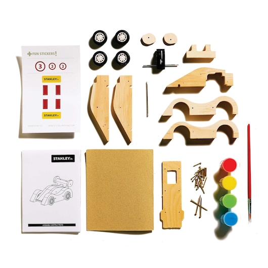 Top-down view of STANLEY wooden race car kit with wheels, paint, brush, stickers, sandpaper, and assembly instructions