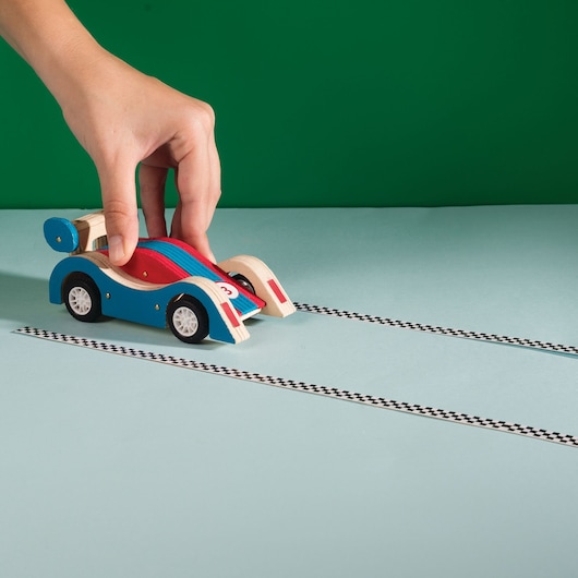 STANLEY JK030-SY toy race car in blue and red held by hand on light blue surface, side angle.