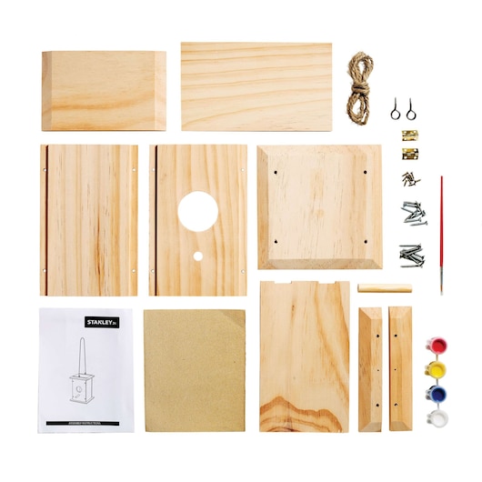 Stanley birdhouse kit top-down view with unassembled wood pieces, screws, rope, sandpaper, paint, brush, instructions.