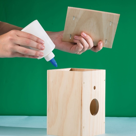 STANLEY K033-SY wood glue applied to birdhouse assembly, product photography against green background.