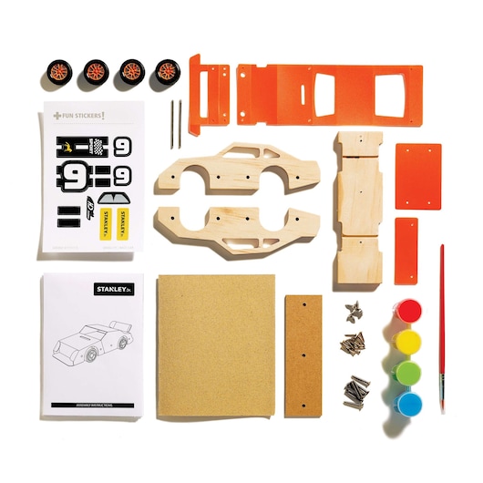 STANLEY OK002-SY race car kit with wood, orange plastic parts, wheels, stickers, paint, brush, and assembly guide.