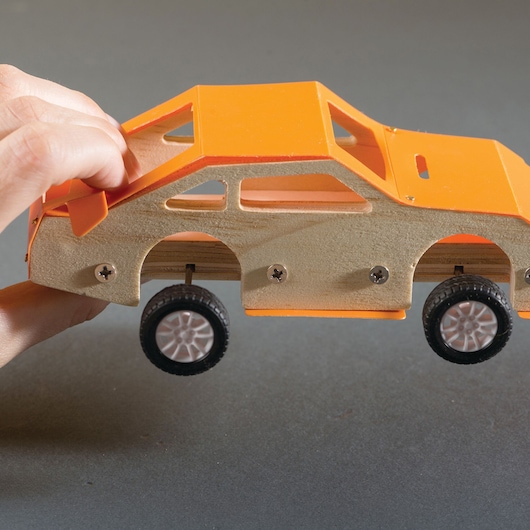 STANLEY OK002-SY wooden toy car with orange accents, side view, held by hand.