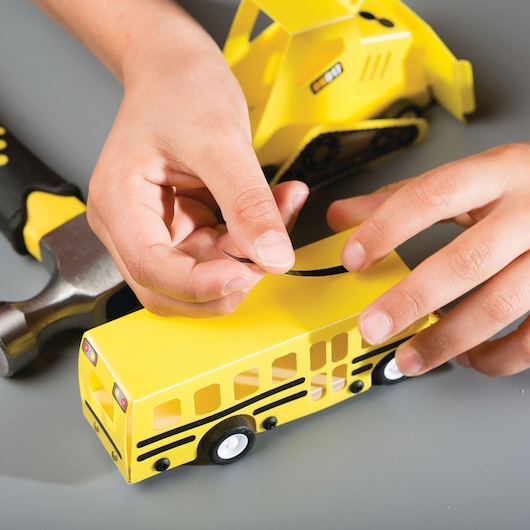 STANLEY OK015-SY toy yellow bus and bulldozer on table, child placing sticker on bus, close-up photography.