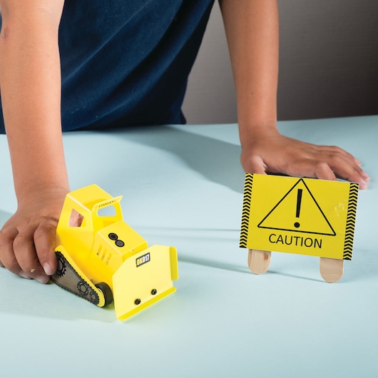 STANLEY OK017-SY toy construction vehicle and caution sign on a table, child's hands visible.