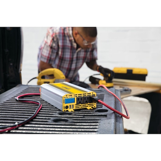 STANLEY PI1000S power inverter with yellow and silver casing on truck bed, connected with red and black wires.