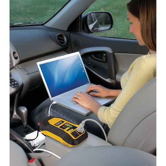 STANLEY PI500S power inverter charging a laptop on a car seat, interior view, with visible cables.