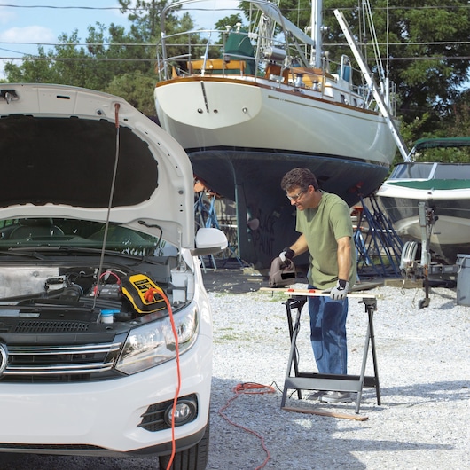 STANLEY PI500S portable power inverter on car engine, outdoor setting near boats, front angle.