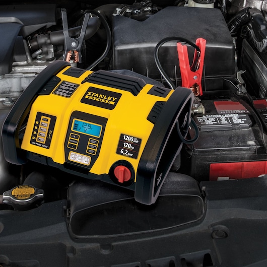 STANLEY PP1DCS battery jump starter with digital display and clamps on a car engine.