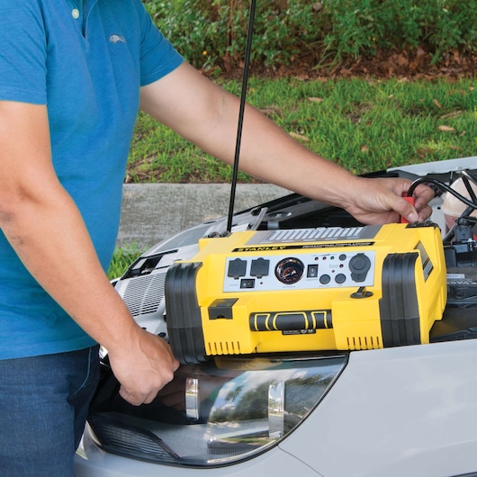 STANLEY PPRH5 portable power station connected to car battery under hood in outdoor setting.