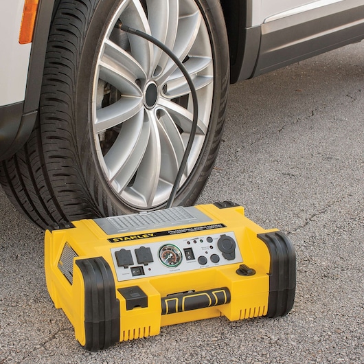 STANLEY PPRH5 portable power station inflating a car tire, yellow and black unit on pavement, front angle.