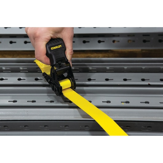 STANLEY S10002 yellow ratchet tie down strap in use on metal rail, close-up photography.