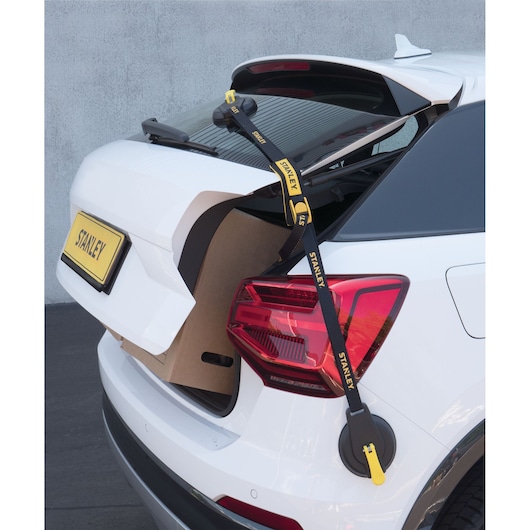 STANLEY S4002 tie-down strap securing hatchback car trunk carrying large box, shown from rear angle.