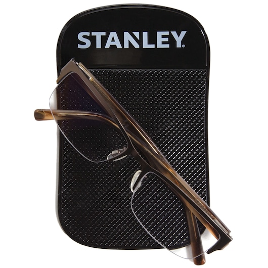 Stanley dashboard anti-slip pad with black textured surface, holding brown eyeglasses, top-down view.
