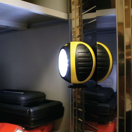 Photo of STANLEY SB01AL round yellow and black LED work light mounted on a metal shelf in a storage area.