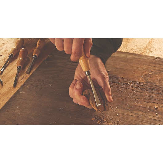 Photo of STANLEY STHT16863 wood chisel in hand carving wood, with other chisels on workbench.