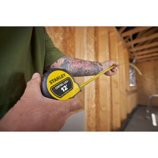 Photo of STANLEY STHT37242 tape measure in use, yellow and black, measuring inside a wooden framed room.