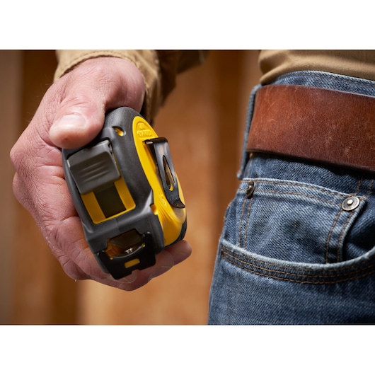 STANLEY STHT37244 tape measure held in hand near blue jeans and brown leather belt, close-up view.