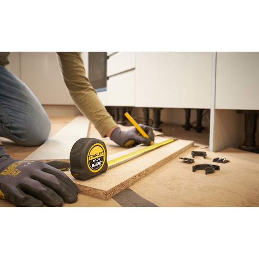 STANLEY STHT39526 tape measure on wood, person wearing gloves marking with pencil; photography of measuring tools.