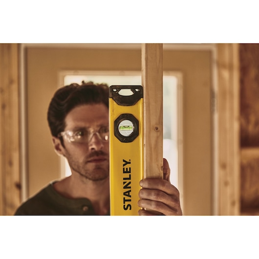 STANLEY STHT42496 level tool in use, held vertically against a wooden stud in a construction setting.