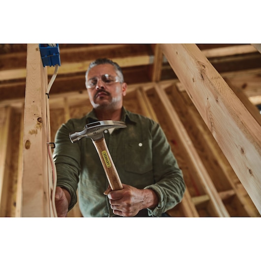 Stanley STHT51456 claw hammer with wooden handle held by person in green shirt at construction site.
