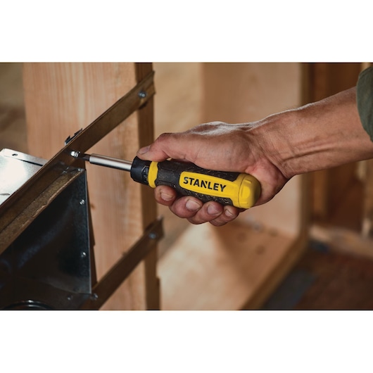 Stanley STHT60129 screwdriver being used to fasten a screw into a metal bracket on wooden framing.