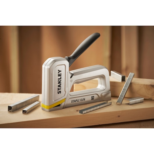 Stanley STHT70150 staple gun with black handle on wood, surrounded by metal staples, side angle photo.