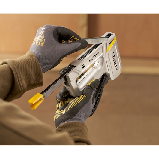 Photo of STANLEY STHT70150 staple gun being loaded with staples by a gloved hand.