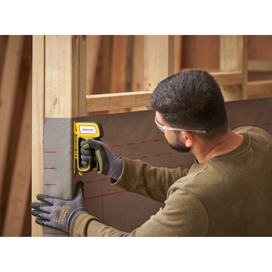 STANLEY STHT70440 stapler tool in use attaching material to wooden frame, close side angle.