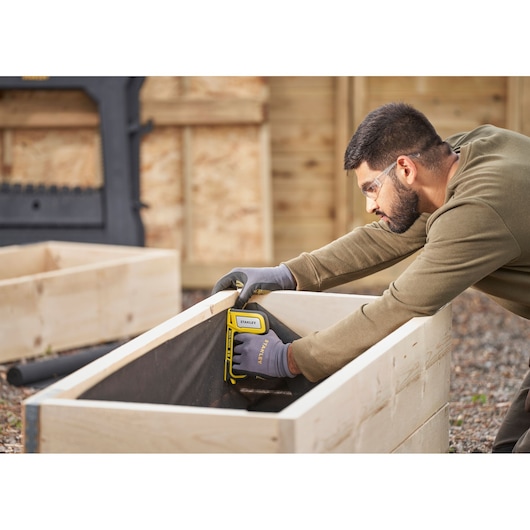 Photo of STANLEY STHT70440 staple gun used on wooden planter outdoors.