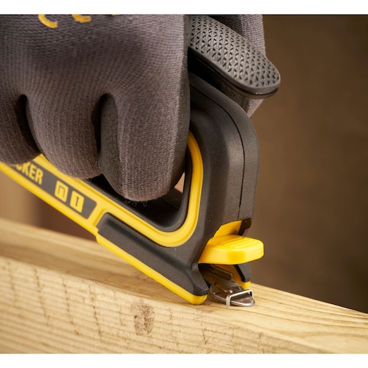 STANLEY STHT70440 hand stapler in use on wood, close-up side angle, person wearing black gloves.