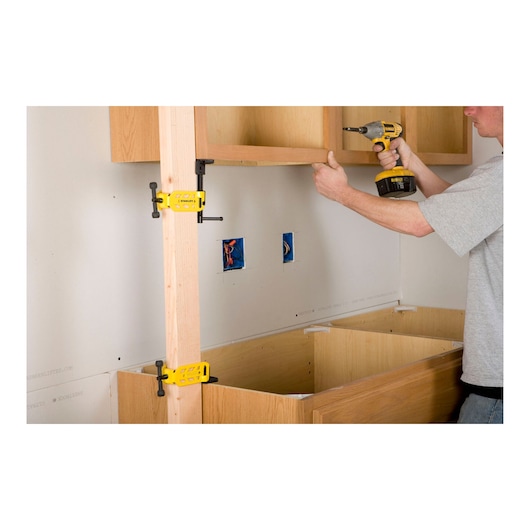 STANLEY STHT83166 clamp holding wooden frame during cabinet installation, side angle photo.