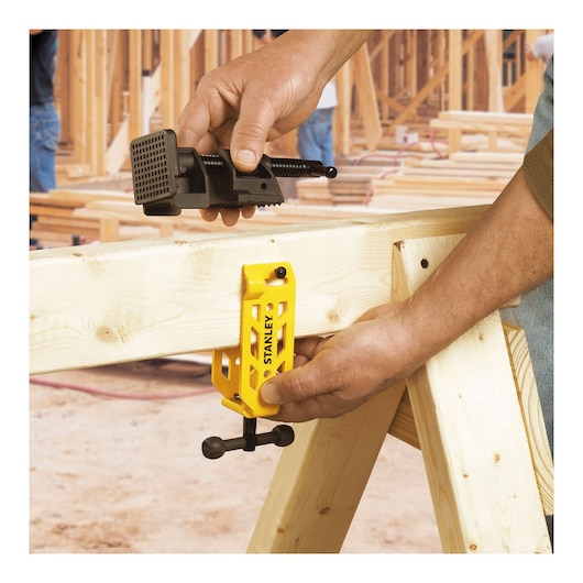 STANLEY STHT83166 yellow woodworking clamp in use on wooden beam at construction site, close-up.