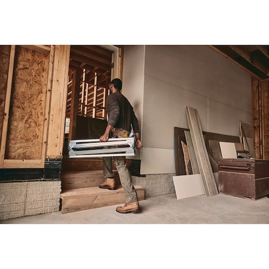 STANLEY STST11154 folding sawhorse carried by person at construction site with exposed wood framing.