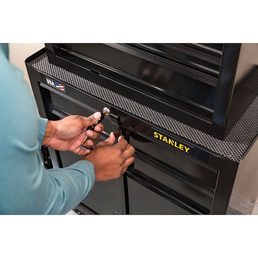 Photo of a person locking a black STANLEY STST22656BK tool chest, showing the brand logo and textured surface.