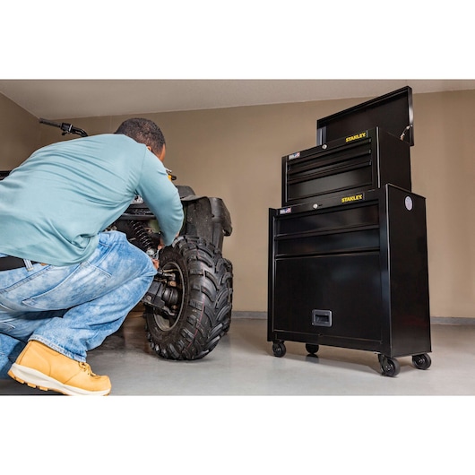 STANLEY STST22656BK black rolling tool chest with open top drawer, shown in a garage next to a person repairing an ATV.