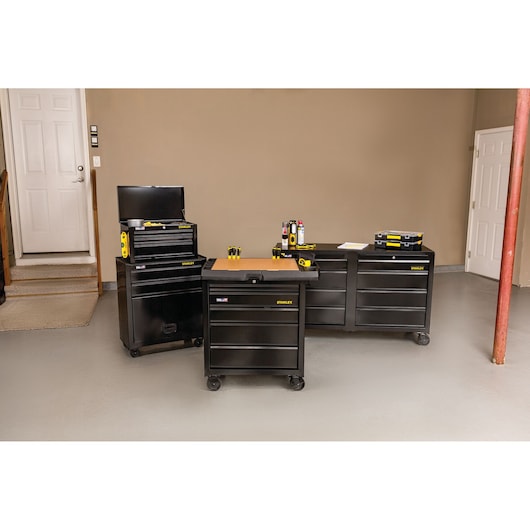 STANLEY STST22656BK black rolling tool chest and cabinet with wood top, shown in a garage with tools on top, front angle.