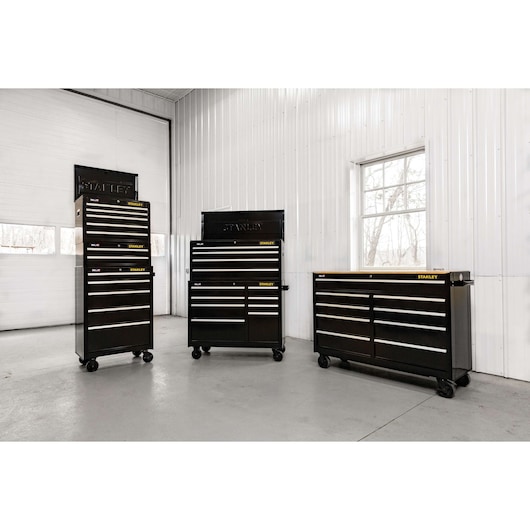 Photo of three STANLEY STST22657BK black rolling tool chests with multiple drawers, shown in a workshop.