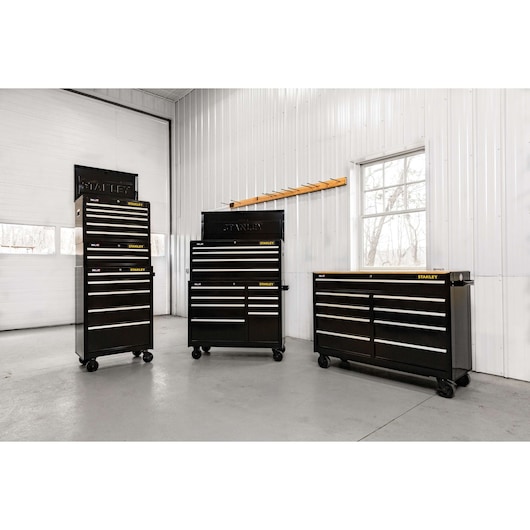 STANLEY STST22753BK black steel tool chests and cabinets with multiple drawers, photographed in a workshop setting.