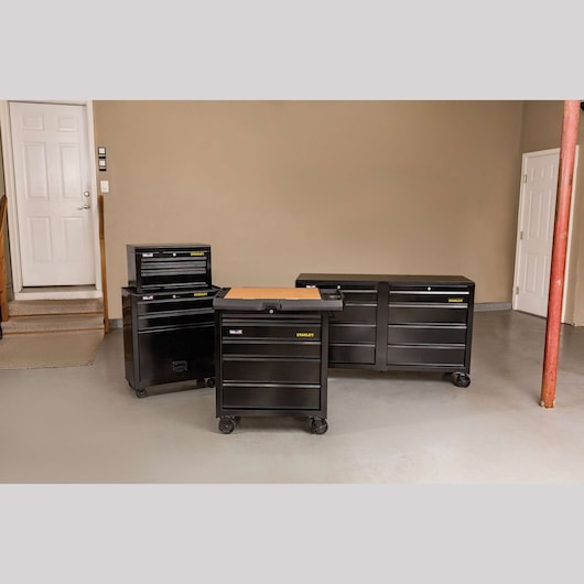 STANLEY STST23151BK black rolling tool chests with multiple drawers, shown in a garage, front angle.