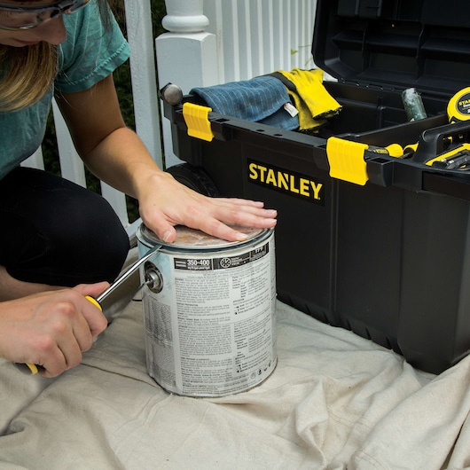 Photo of STANLEY STST33031 tool box with open lid, tools and gloves visible, next to a person opening a paint can.