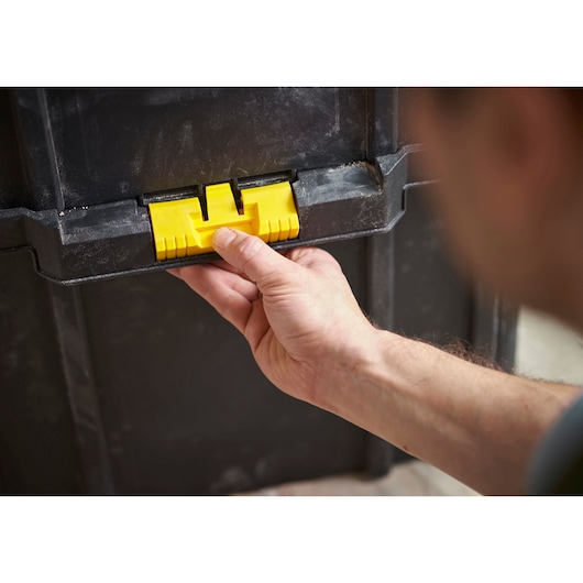 STANLEY STST60500 storage box yellow latch close-up, hand opening black container.