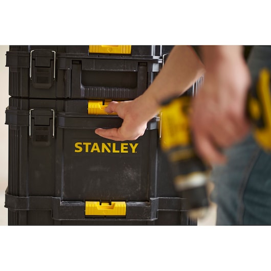 Stanley STST60500 black and yellow tool box with person opening latch, photography close-up.