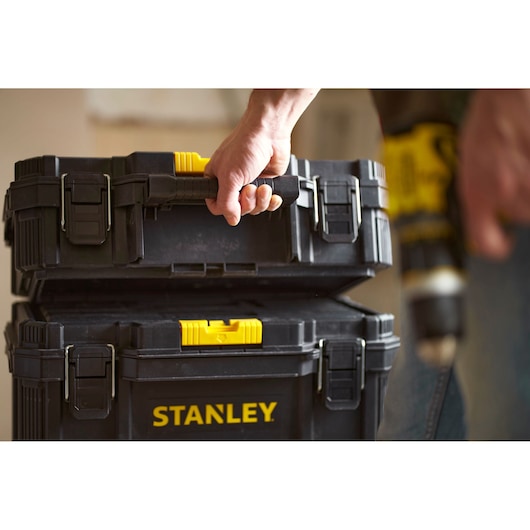 Photo of STANLEY STST60500 black and yellow stackable tool boxes, one being carried by a hand.