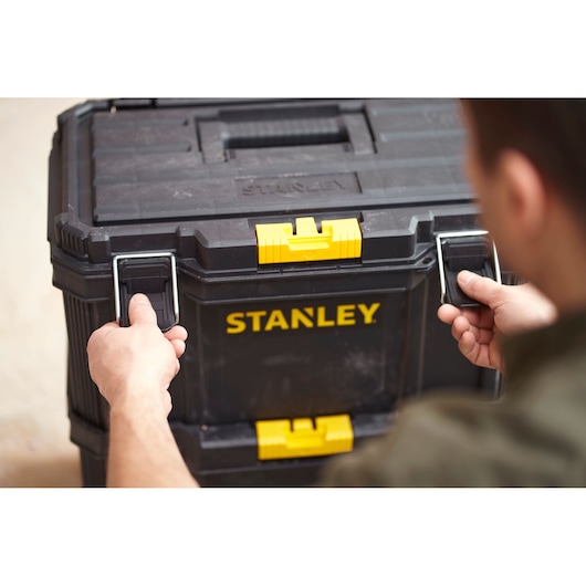 STANLEY STST60500 black tool chest with yellow latches, front angle, hands opening metal handles.