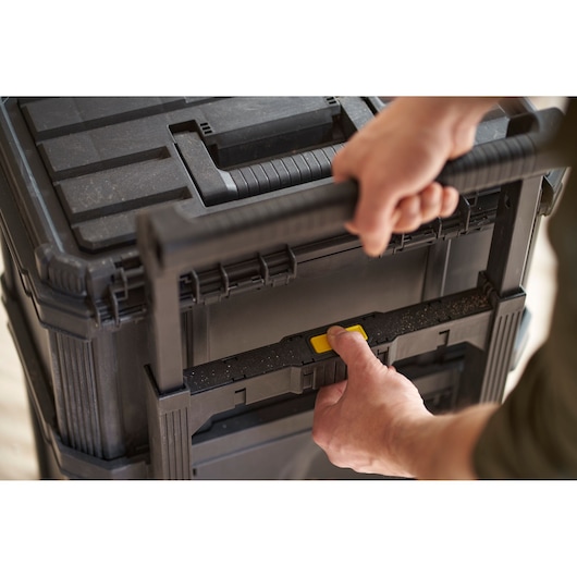 STANLEY STST60500 storage box with black handle, close-up of hands pressing yellow button on handle.